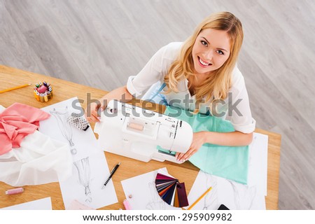 Fashion designer at work. Top view of cheerful young woman sewing while sitting at her working place in workshop