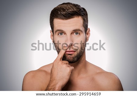 Digging for gold. Portrait of handsome young shirtless man picking his nose while standing against grey background