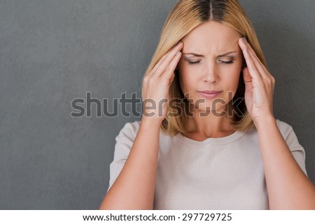I need some painkillers. Depressed mature woman touching forehead and keeping eyes closed while standing against grey background