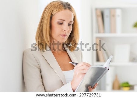 Everything must be in order. Confident mature businesswoman writing in note pad while leaning at the wall