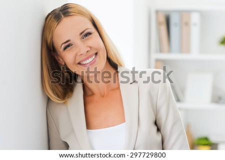 Face of job satisfaction. Beautiful mature businesswoman looking at camera and smiling while leaning at the wall