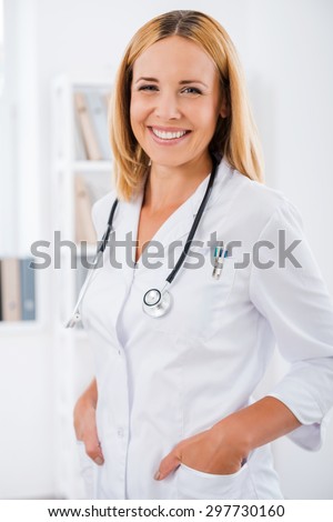 She is a dedicated doctor. Smiling female doctor in white uniform looking at camera and holding hands in pockets