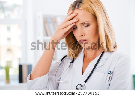Headache at the hospital. Frustrated female doctor in white uniform touching forehead and keeping eyes closed
