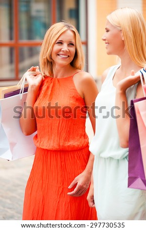 Shopping with her best friend. Cheerful mother and her daughter carrying shopping bags and looking at each other while walking outdoors