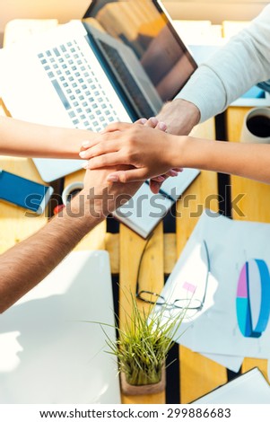 Team spirit. Top view of business people holding hands clasped upon the wooden desk