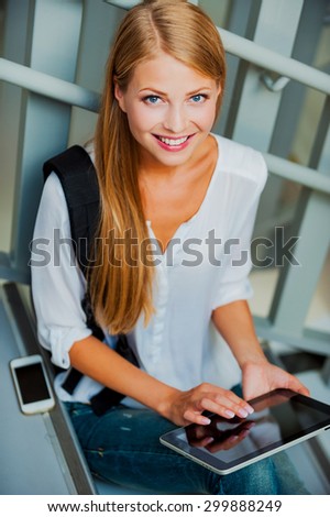 Technologies makes study easier. Top view of smiling young woman holding digital tablet and looking at camera while sitting on the stairs