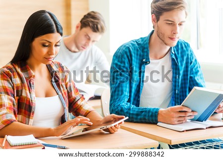 Full concentration. Three concentrated young students studying while sitting at their desks in the classroom