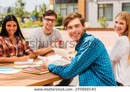 Quick meetin. Group of happy young people looking at camera and smiling while sitting at the wooden desk outdoors