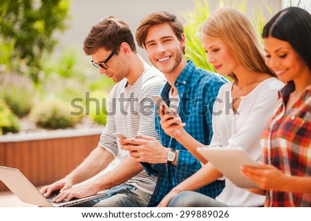Living a digital life. Group of young people holding different digital devices while man looking at camera and holding mobile phone