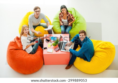 Creative work space. Top view of four cheerful young people working together and looking up while sitting at the colorful bean bags
