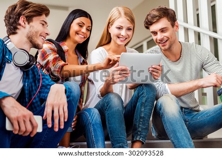 Look at this! Low angle view of four young people looking at digital tablet while sitting at the staircase