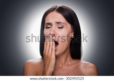 Feeling sleepy. Portrait of bored young shirtless woman covering mouth by hand and yawning while standing against grey background