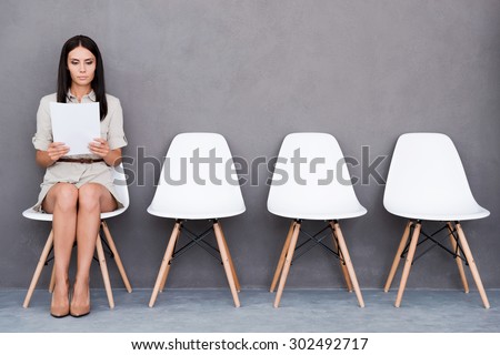 Waiting for interview. Confident young businesswoman holding paper while sitting on chair against grey background