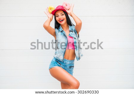 Adding some fun to her day. Cheerful young women holding donuts above her head and smiling while standing against the garage door