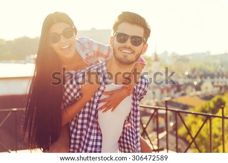 Young and in love. Happy young man carrying his girlfriend on shoulders while having fun together on the roof