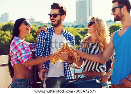 Party on! Group of happy young people clinking glasses with beer and barbecuing while standing on the roof