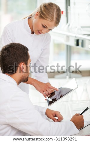 She needs an expert advise. Side view of confident young female scientist showing something on her digital tablet to her colleague while working together in the laboratory