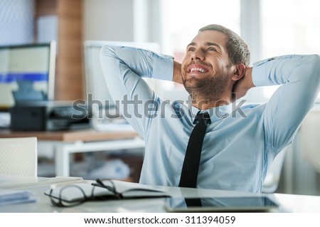 Job satisfaction. Cheerful businessman in formalwear holding head in hands while sitting at his desk in the office