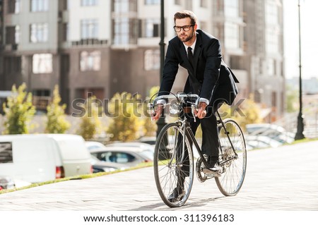 Cycling is the way to progress! Full length of handsome young businessman looking forward while riding on his bicycle