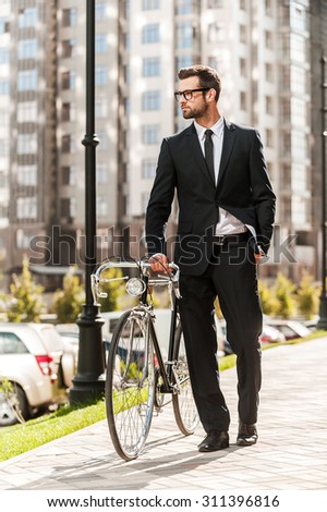 Getting to work by bike today. Full length of handsome young businessman rolling his bicycle while walking outdoors