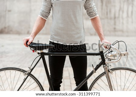 Proud of his bike. Close-up of young man holding hands on his bicycle while standing outdoors