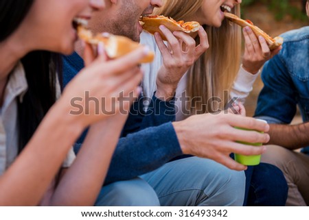 Time for pizza! Group of young people eating pizza while sitting outdoors