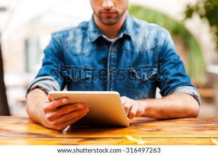 The whole world in one touch. Cropped image of young man working on digital tablet while sitting at the wooden table outdoors