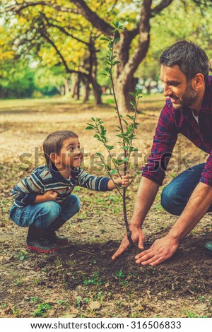 This tree will grow with you! Playful little boy helping his father to plant the tree while working together in the garden