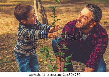 Planting a family tree. Happy young man planting a tree while his little son helping him