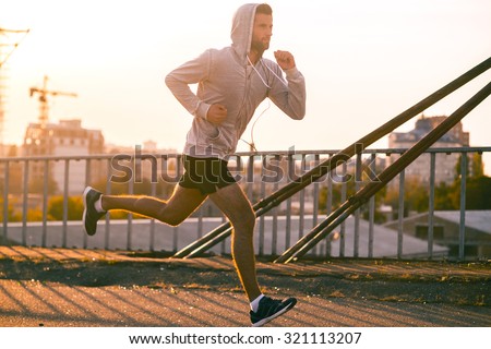 Moving to his goal. Side view of confident young man running along the bridge