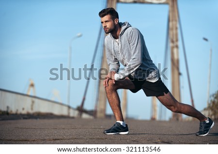 Important stretching. Full length of handsome young man stretching his body before running while standing on the bridge