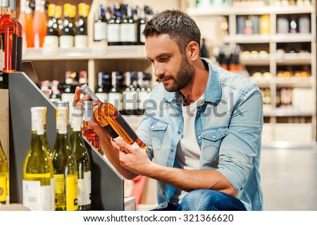 This is perfect wine! Handsome young man holding bottle of wine while standing in a wine store