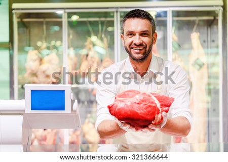 The best quality meat for you. Cheerful young butcher stretching out slice of meat and looking at camera while standing at supermarket checkout