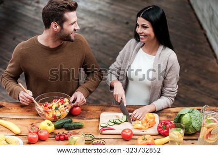Enjoying cooking together. Top view of beautiful young couple preparing healthy salad together and smiling