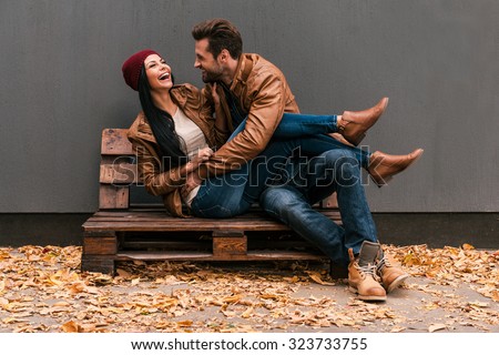 Carefree time together. Beautiful young couple having fun together while sitting on the wooden pallet together with grey wall in the background and fallen leaves on ht floor