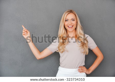 She never gives bad advices. Cheerful young blond hair woman pointing away and looking at camera while standing against grey background