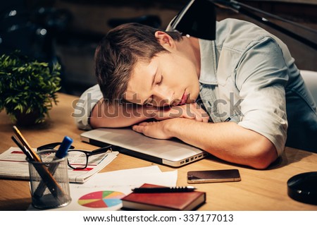 Too much work. Young man sleeping at his working place while leaning his head on the laptop