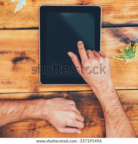 All the world in one touch. Close-up of man holding his finger on digital tablet while sitting at the wooden table outdoors
