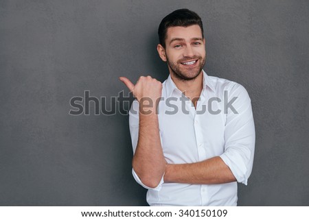 Pointing copy space. Handsome young man pointing copy space and smiling while standing against grey background