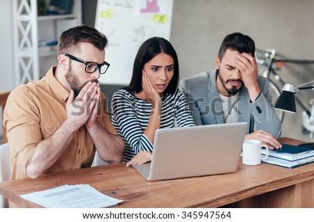 Oh no! Three frustrated young business people in smart casual wear looking at the laptop and expressing negativity