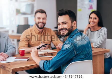Enjoying good working day together. Group of confident business people in smart casual wear sitting at the table and smiling