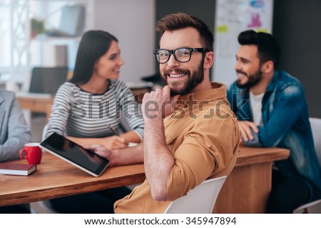 Feeling confident in my team. Group of business people in smart casual wear discussing something while one man holding digital tablet and looking over shoulder with smile