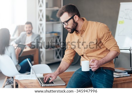 IT professional at work. Confident young man working on laptop while his colleagues talking in the background