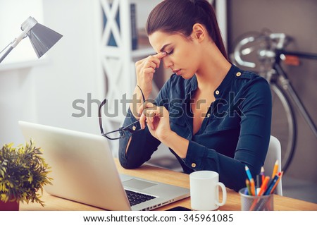 Feeling tired and stressed. Frustrated young woman keeping eyes closed and massaging nose while sitting at her working place in office