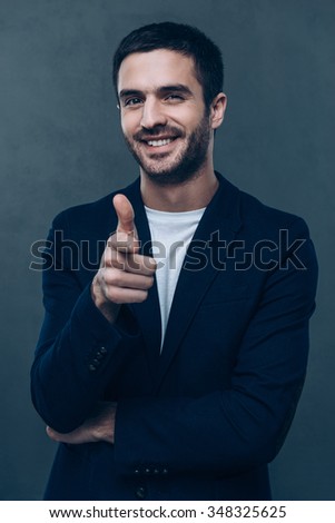 You are awesome! Cheerful young man pointing you and looking at camera while standing against grey background