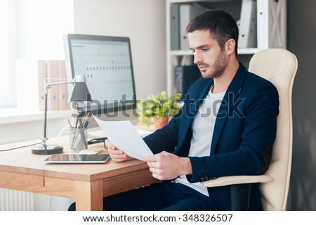 Man examining documents. Side view of confident young man examining document while sitting at his working place in office