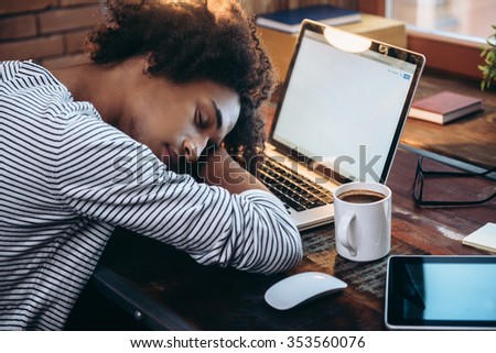 Quick nap. Side view of young African man sleeping on laptop with eyes closed while sitting at his working place