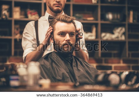 Looking amazing. Close-up of hairdresser checking symmetry of haircut of his client at barbershop