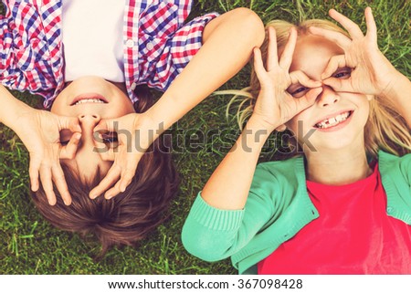 Summer time fun. Top view of two cute little children making faces and smiling while lying on the green grass together