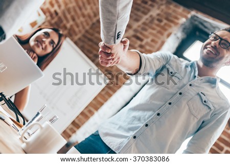 Congratulations! Low angle view of two men shaking hands while their coworker sitting at the table in office